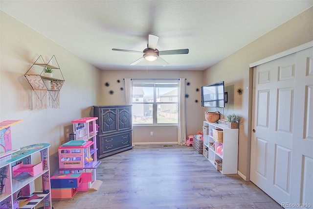 recreation room featuring a textured ceiling, ceiling fan, and light hardwood / wood-style floors