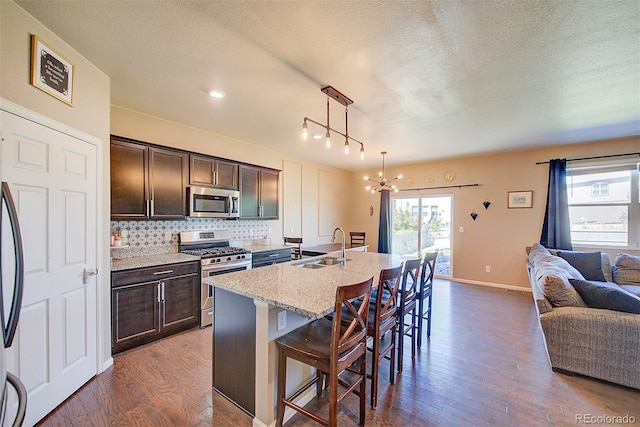 kitchen with pendant lighting, a breakfast bar area, light stone countertops, a kitchen island with sink, and appliances with stainless steel finishes