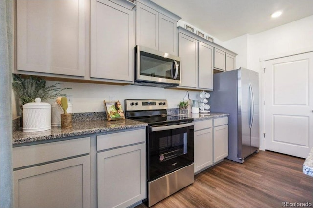 kitchen featuring dark wood-type flooring, appliances with stainless steel finishes, gray cabinets, and dark stone counters