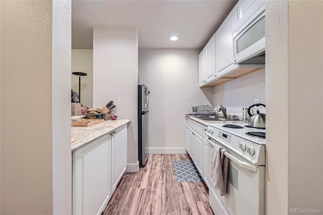 kitchen with white appliances, white cabinets, sink, light hardwood / wood-style flooring, and light stone countertops