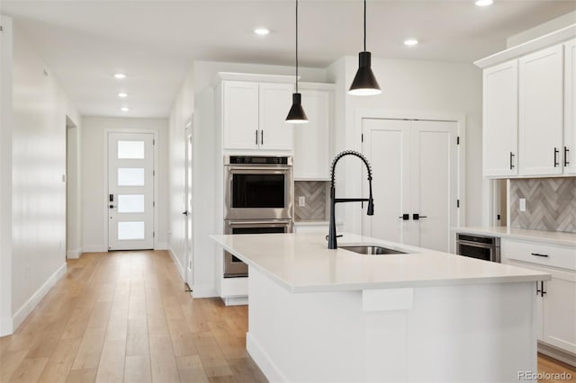 kitchen featuring white cabinetry, hanging light fixtures, double oven, and a center island with sink