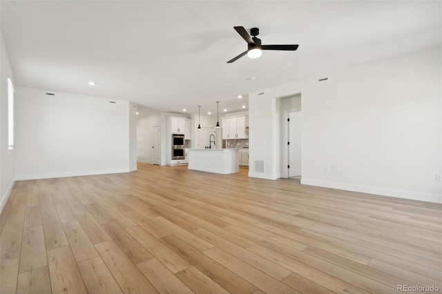 unfurnished living room with sink, ceiling fan, and light wood-type flooring