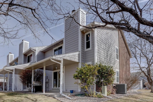 rear view of house with central air condition unit, covered porch, and a chimney