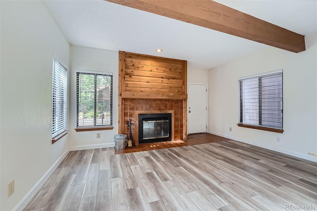 unfurnished living room with hardwood / wood-style floors, beam ceiling, a tiled fireplace, and wood walls