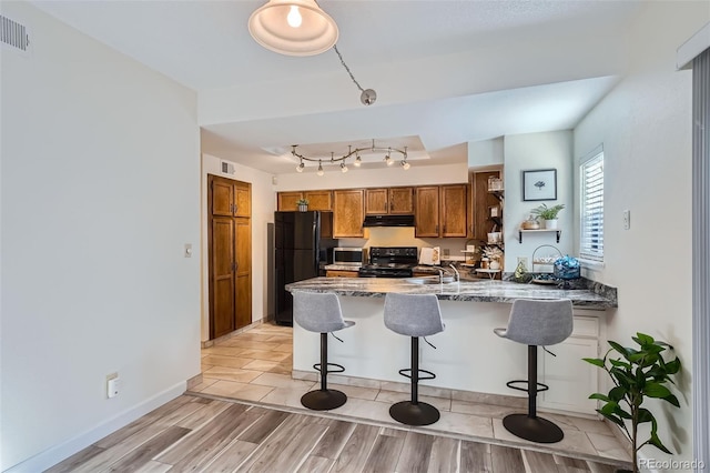 kitchen featuring black refrigerator, light hardwood / wood-style floors, rail lighting, and range