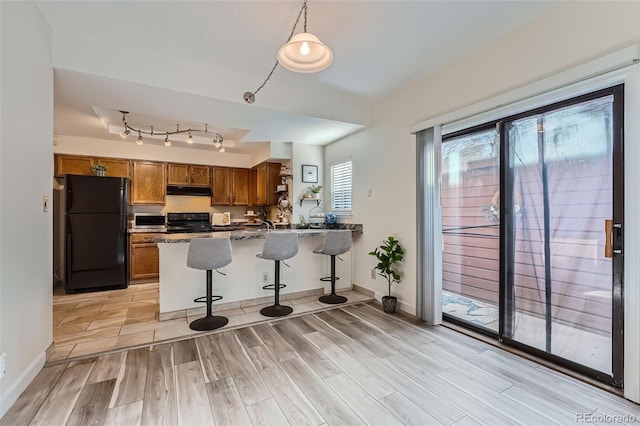 kitchen featuring a breakfast bar, black refrigerator, range, track lighting, and kitchen peninsula