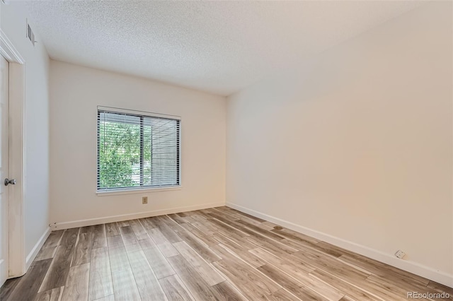 spare room with light wood-type flooring and a textured ceiling