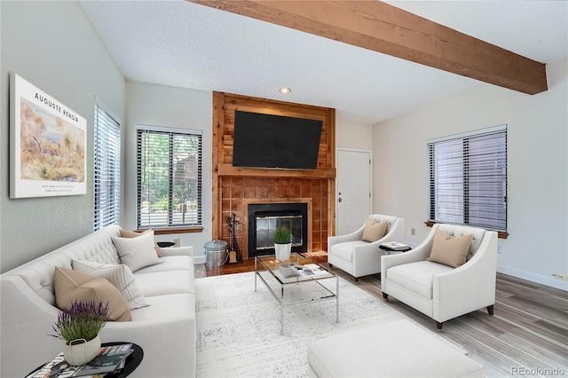 living room with beam ceiling, hardwood / wood-style flooring, and a tiled fireplace