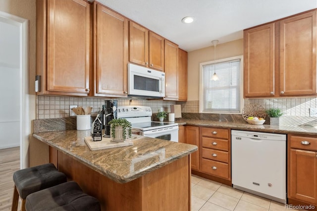 kitchen with dark stone countertops, hanging light fixtures, white appliances, and a breakfast bar