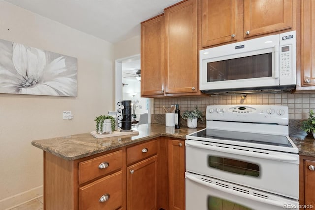 kitchen featuring tasteful backsplash, dark stone counters, light tile patterned floors, kitchen peninsula, and white appliances