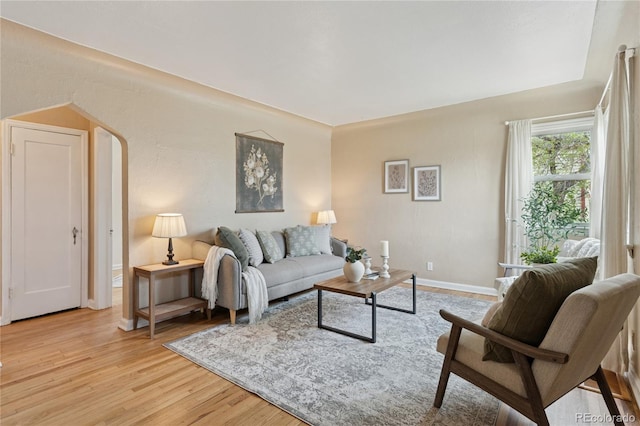 living room featuring arched walkways, baseboards, and light wood-style flooring