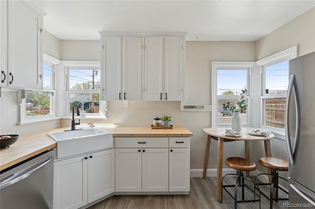 kitchen with a sink, butcher block countertops, light wood-style flooring, stainless steel appliances, and a wealth of natural light