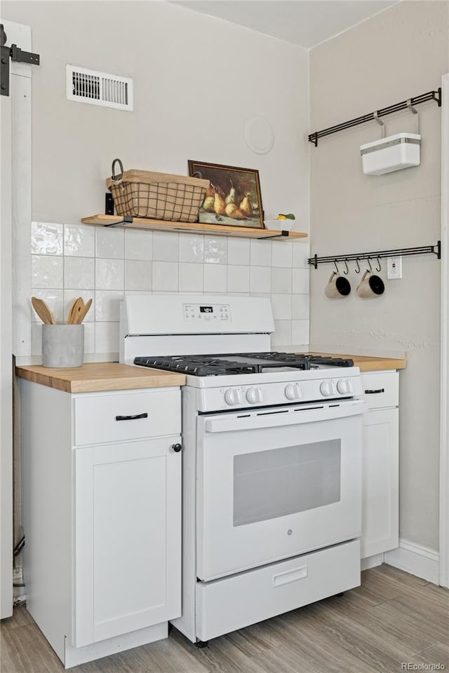 kitchen featuring visible vents, butcher block counters, light wood-type flooring, white cabinets, and white gas range oven