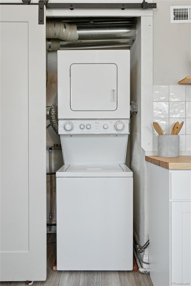 laundry room featuring laundry area, stacked washer / dryer, visible vents, a barn door, and wood finished floors
