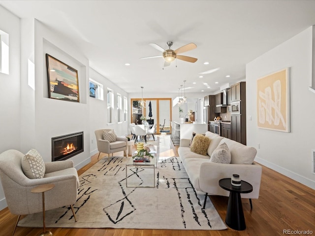 living area featuring recessed lighting, a ceiling fan, baseboards, light wood-type flooring, and a glass covered fireplace