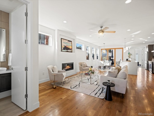 living area with baseboards, wood finished floors, a glass covered fireplace, and recessed lighting