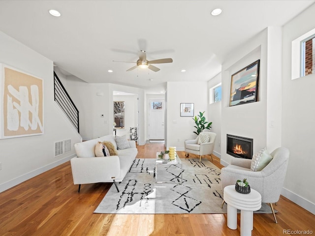 living area featuring recessed lighting, wood finished floors, visible vents, stairs, and a glass covered fireplace