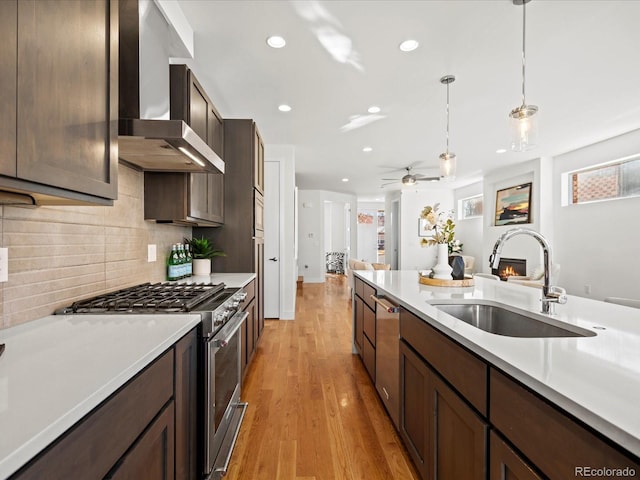 kitchen featuring wall chimney exhaust hood, hanging light fixtures, light countertops, high end stove, and a sink