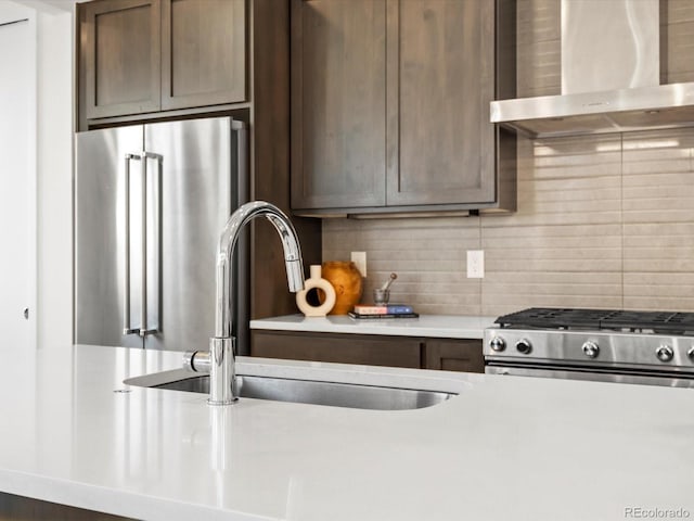kitchen with light countertops, decorative backsplash, appliances with stainless steel finishes, a sink, and wall chimney exhaust hood