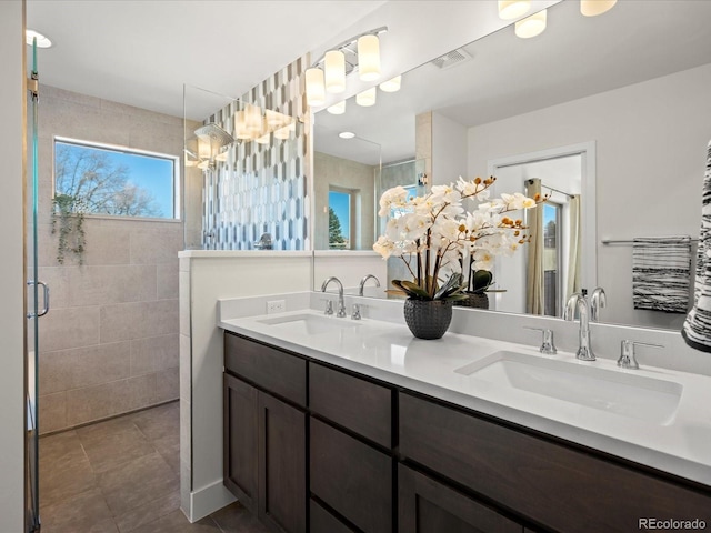 bathroom featuring double vanity, tiled shower, a sink, and tile patterned floors