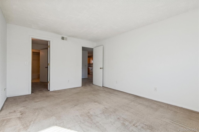 unfurnished bedroom featuring light colored carpet, a textured ceiling, and a walk in closet