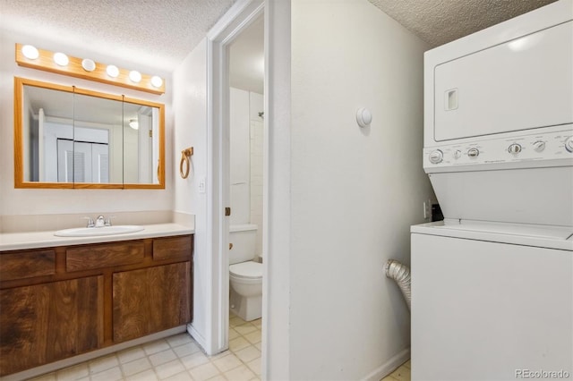 bathroom with stacked washer / drying machine, toilet, a textured ceiling, and vanity