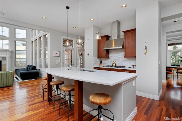 8044 E 24th Ave, Denver, CO 80238 - kitchen with wall chimney range hood, gas cooktop, dark wood-style flooring, a kitchen breakfast bar, and decorative backsplash