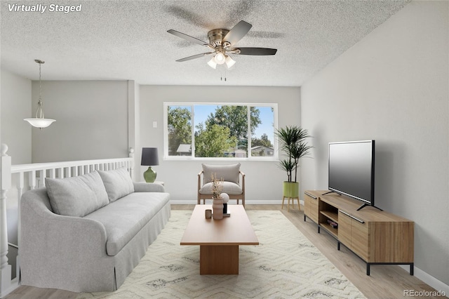 living room featuring light wood-type flooring, a textured ceiling, and ceiling fan