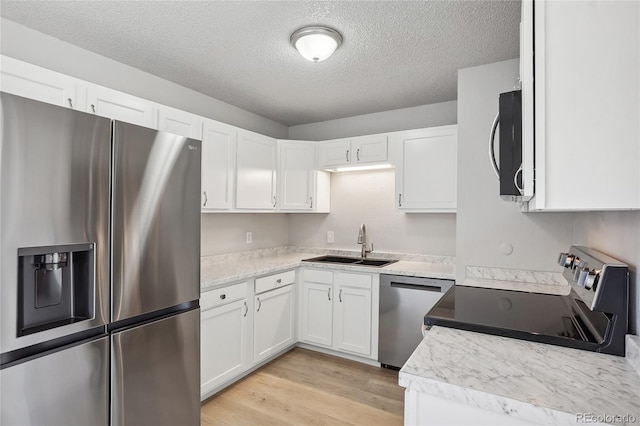 kitchen with light hardwood / wood-style floors, a textured ceiling, sink, white cabinets, and appliances with stainless steel finishes