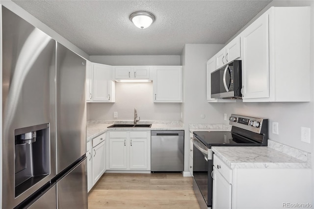 kitchen with light wood-type flooring, a textured ceiling, sink, white cabinetry, and appliances with stainless steel finishes