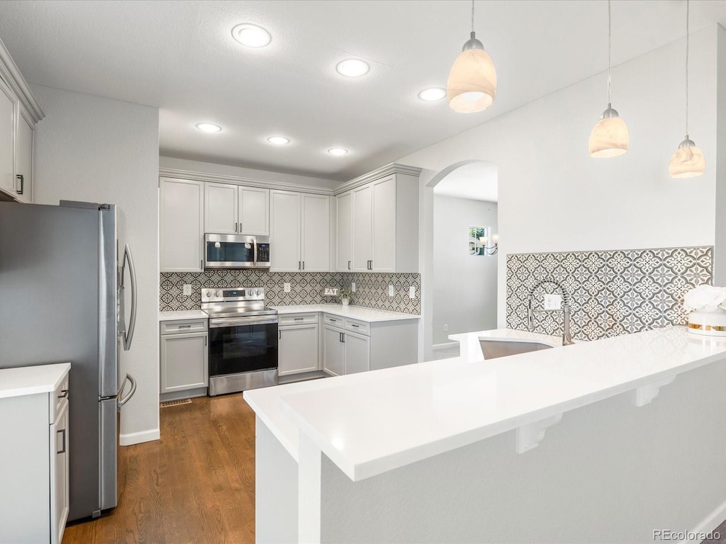 kitchen featuring stainless steel appliances, pendant lighting, a kitchen bar, and kitchen peninsula