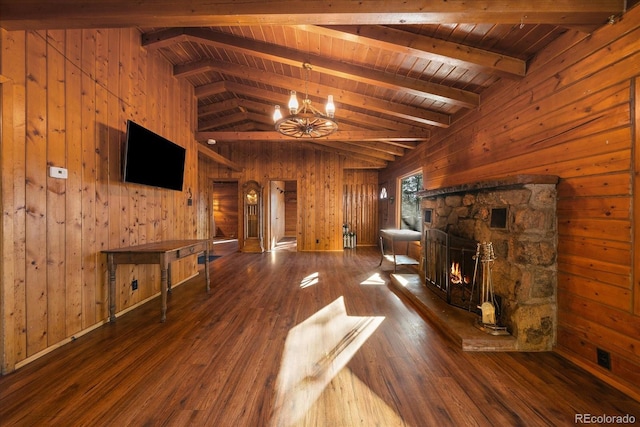 unfurnished living room featuring vaulted ceiling with beams, a stone fireplace, a notable chandelier, wooden walls, and wood finished floors