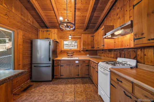 kitchen featuring wooden walls, under cabinet range hood, visible vents, white gas range oven, and freestanding refrigerator