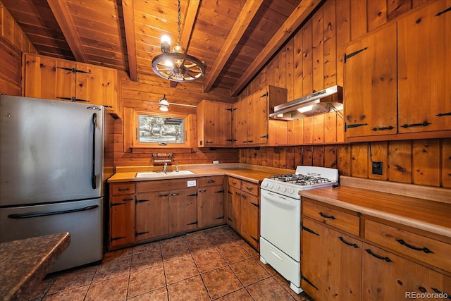 kitchen with freestanding refrigerator, white range with gas cooktop, wooden walls, a sink, and under cabinet range hood