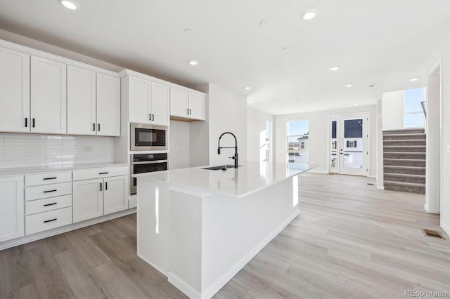 kitchen with stainless steel oven, white cabinets, sink, an island with sink, and built in microwave