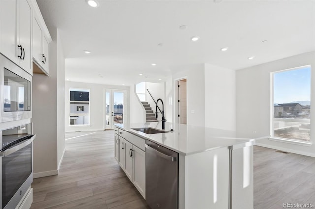 kitchen with a kitchen island with sink, sink, light hardwood / wood-style flooring, white cabinetry, and stainless steel appliances