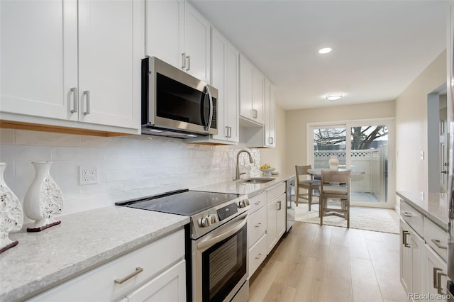 kitchen with light wood-style flooring, white cabinetry, appliances with stainless steel finishes, a sink, and backsplash