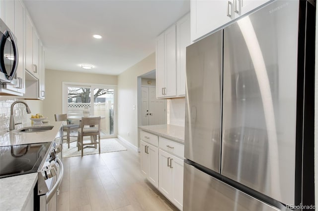 kitchen with stainless steel appliances, tasteful backsplash, white cabinets, and a sink