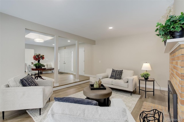 living room featuring light wood finished floors, baseboards, a brick fireplace, and recessed lighting