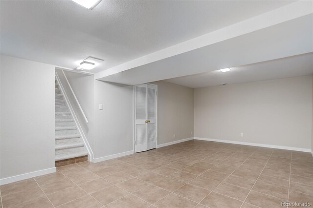 finished below grade area featuring baseboards, light tile patterned flooring, and stairs