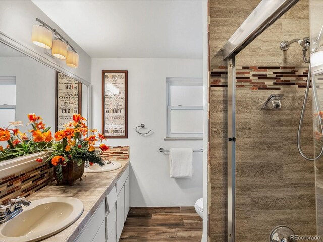 5845 W Portland Dr, Littleton, CO 80128 - bathroom with wood finished floors, backsplash, tiled shower, double vanity, and toilet