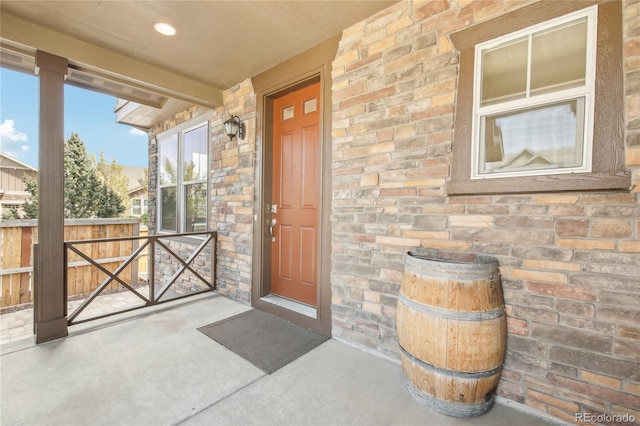 property entrance with fence, a porch, and stone siding