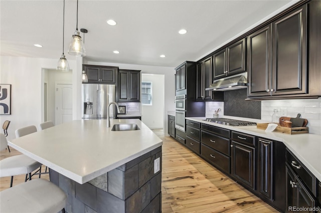 kitchen with a sink, appliances with stainless steel finishes, light countertops, under cabinet range hood, and a breakfast bar area