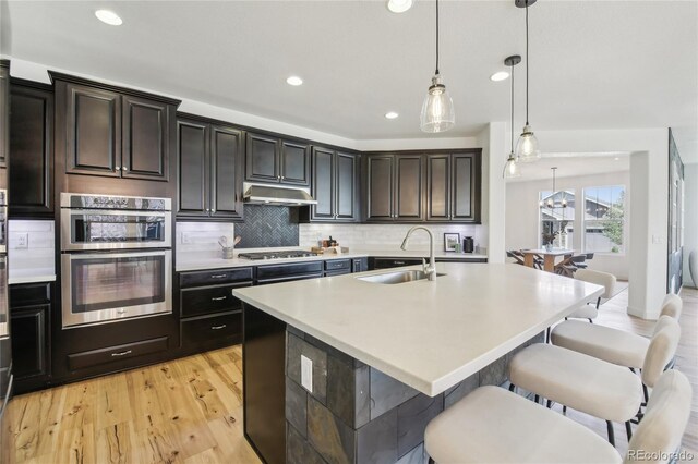 kitchen with recessed lighting, under cabinet range hood, gas cooktop, a sink, and a breakfast bar area