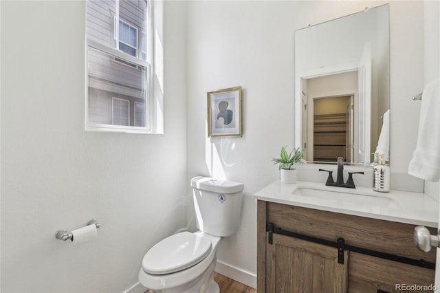 half bath with wood finished floors, vanity, toilet, and baseboards