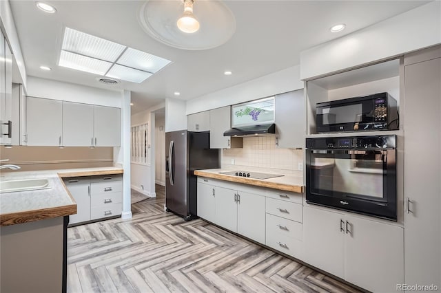 kitchen featuring light parquet flooring, backsplash, black appliances, a skylight, and sink