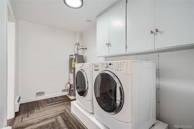 clothes washing area with cabinets, washing machine and clothes dryer, a baseboard radiator, water heater, and dark parquet flooring