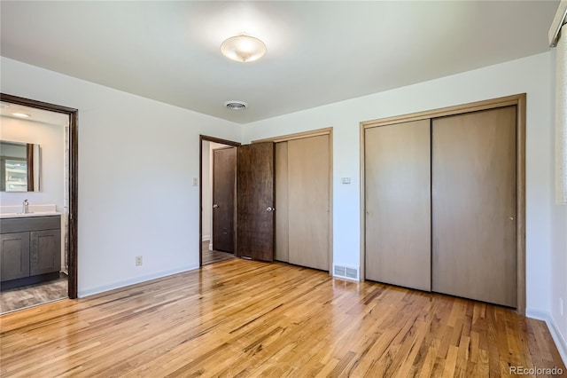 unfurnished bedroom featuring multiple closets, light hardwood / wood-style floors, ensuite bathroom, and sink