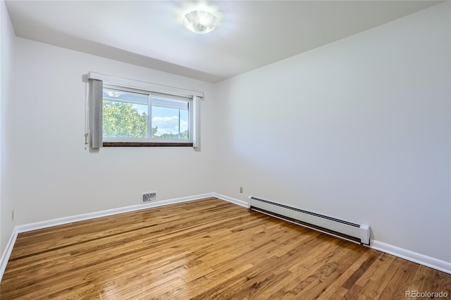 spare room featuring baseboard heating and light hardwood / wood-style flooring