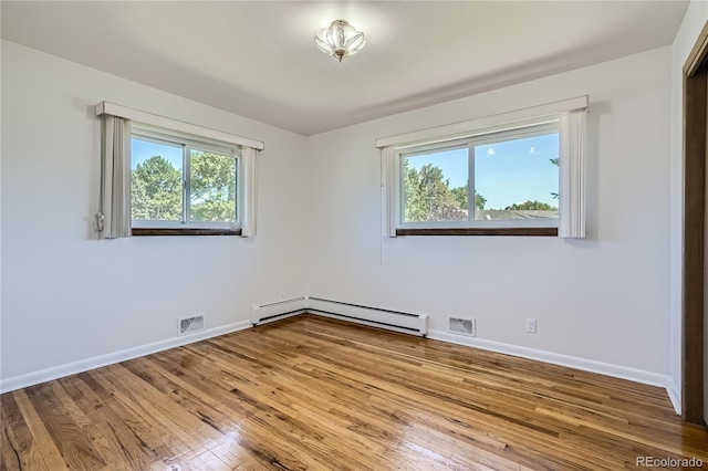 spare room featuring baseboard heating, plenty of natural light, and hardwood / wood-style floors